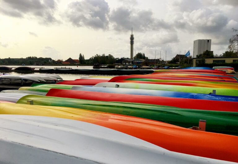 allemaal kajaks op een rij in vrolijke kleuren met op de achtergrond water en de telecom toren van Wormer