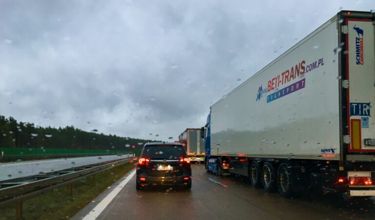 foto van mijn uitzicht uit het autoraam van een snelweg in Polen tegen de avondschemer aan. Rechter rijbaan gevuld met vrachtauto's en voor mij op de linkerbaan een zwarte personenauto.