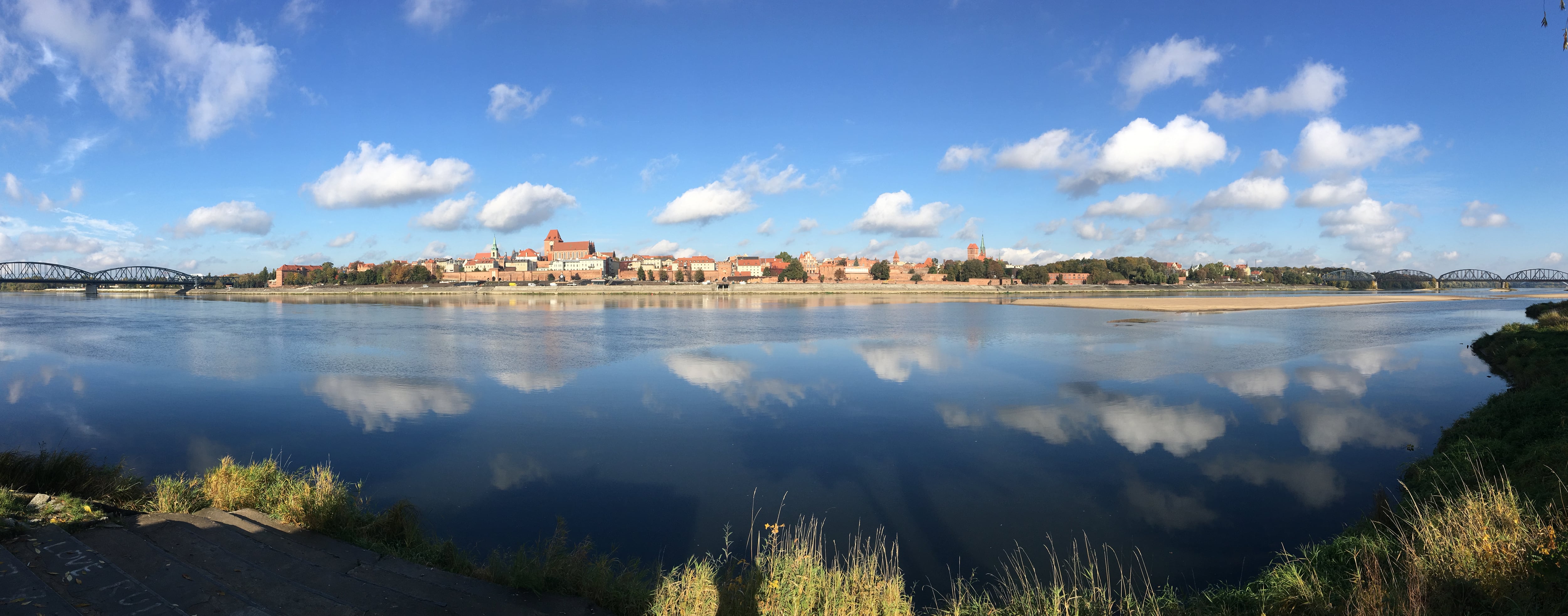 uitzicht op stad Torun in Polen vanaf de andere kant van de rivier de Wisla. De wolken e de heldere blauwe lucht speigelen in het gladde water