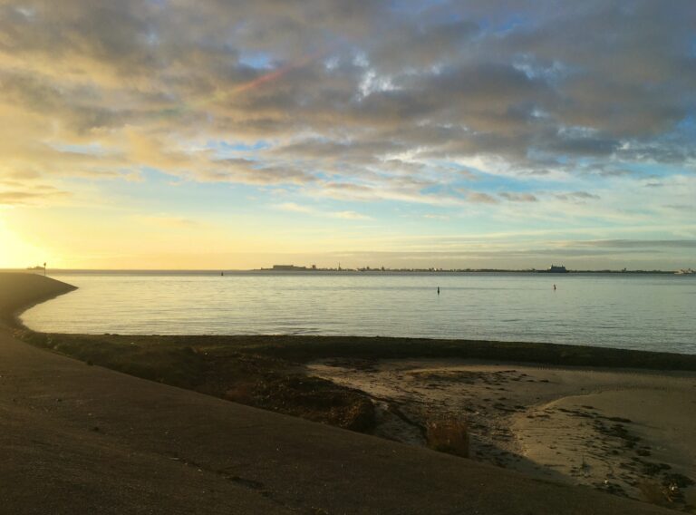 Uitzicht vanaf de haven van Texel op Den Helder met opkomende zon en blauwe lucht met wolkige wolken. De zee is kalm
