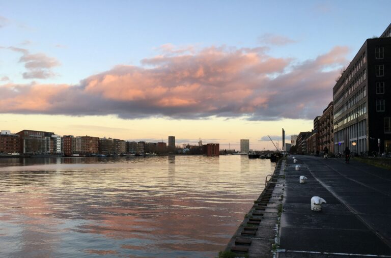 Panorama Veemkade Amsterdam. De lens naar het oosten. Roze wolken van de ondergaande zon en kalm water met de spiegeling van de kleuren.