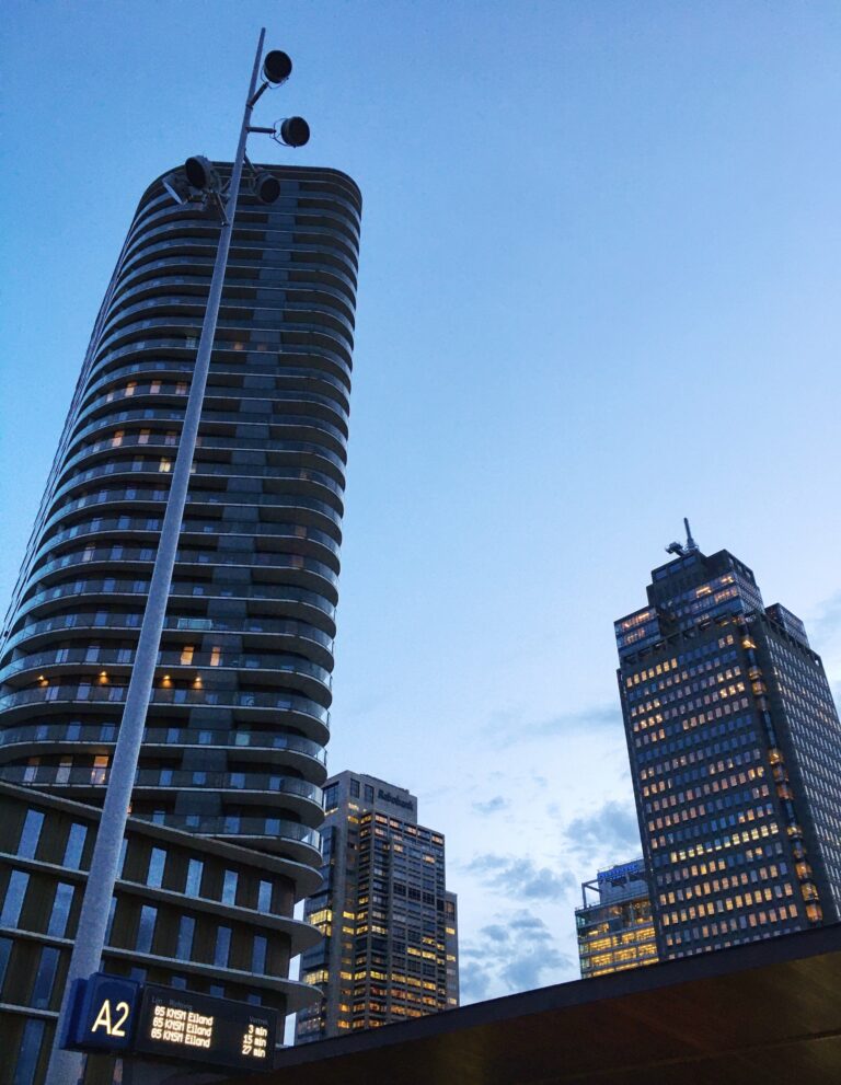 Vier grote flatgebouwen bij het Amstelstation in het het blauwe avondlicht met deels verlichte ramen die oker oplichten.