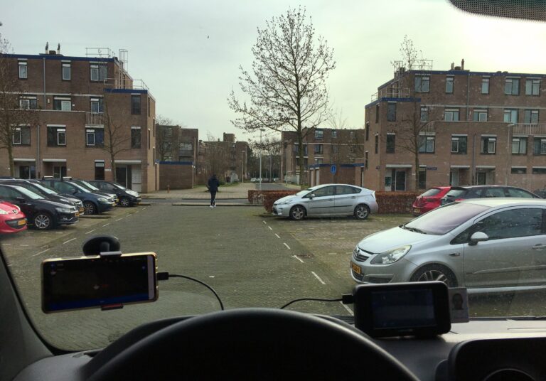 Uitzicht vanuit mijn auto tijdens mijn pauze van het werk. Deze keer een parkeerplaats en wat vierkante appartementencomplexen van 3 verdiepingen en wat kale boompjes tussen al dat steen en autoblik.