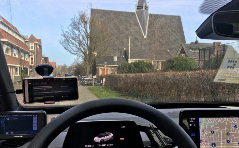 Uitzicht vanuit mijn voorruit van de auto. Rechts van me een heg, links wat huizen uit begin 1900. Ik kijk uit op de Protestantse kerk die gebouwd is in 1937. Groot dak met een torentje in het midden ervan en wat bijgebouwen..
