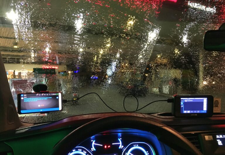 Uitzicht uit mijn voorruit tijdens de pauze bij een tankstation terwijl ik aan de snellader sta. Het regent en de kleuren van de neon lichten maken het een bijzonder schouwspel van licht.