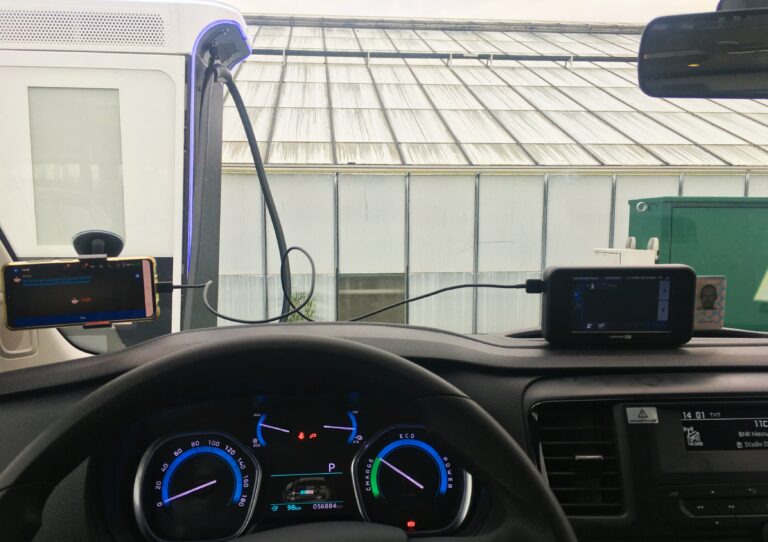 Uitzicht vanuit de voorruit bij een tankstation. Auto staat aan de snellader en ik kijk uit op een kas met melkglas. Dus geen idee wat er in zit.