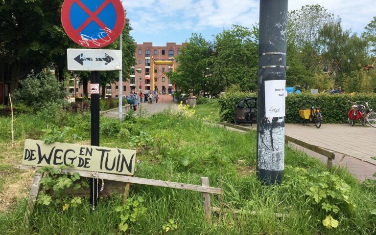 Het begin van het fietspad naar het entrepodok over de Nijlpaardenbrug Heb je borden en een lantaarnpaal. Op paal zit een poster van Loesje met de tekst "Mooi hè, alles".