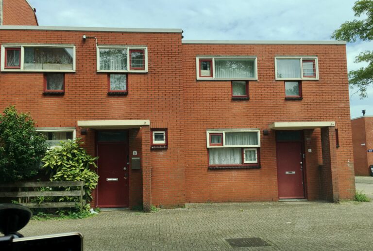 Een rood bakstenen rijtjeshuis met een plat dak en veel kleine raampjes. Doet denken aan een blokkendoos