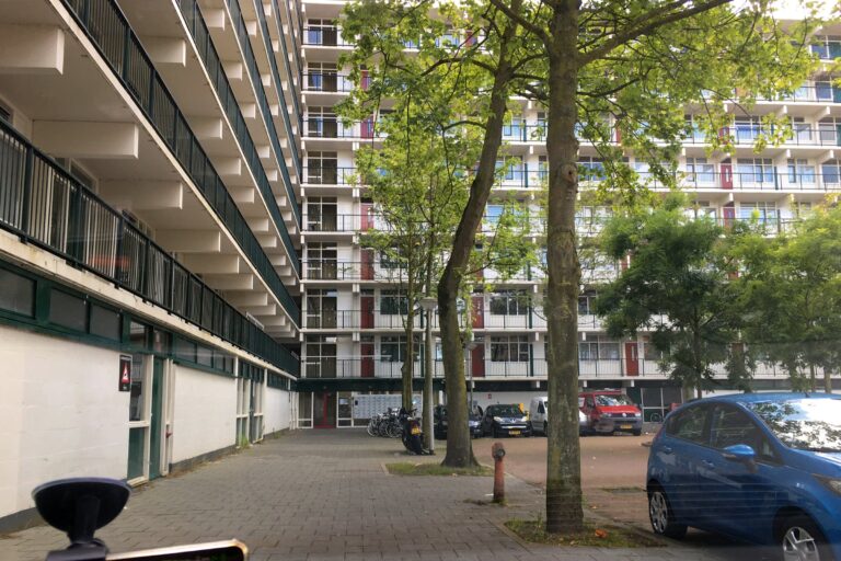 hoekflat uit de jaren '70 van 10 verdiepingen. Recht vooruit is de binnenkant van die hoek. Links is het flatgebouw wat in perspectief naar de hoek gaat en recht voor is de andere helft van de flat. De binnenplaats is een parkeerplaats met wat bomen en wat auto's