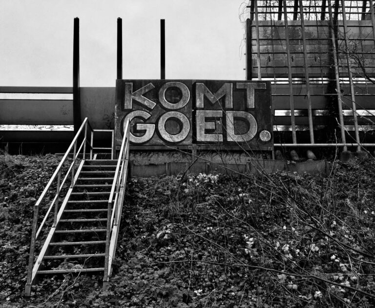 Een graffiti tekst "KOMT GOED" aan de rand van de A10 in Amsterdam. Er leidt een stalen trap naartoe. Waarschijnlijk een nooduitgang vanaf de snelweg.