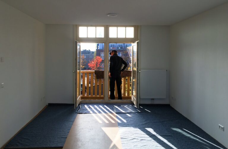 Een lege kamer met een doorkijkje naar het balkon. De balkondeuren staan open en de verhuizer wacht op de eerste spullen. De ochtend zon schijnt heerlijk naar binnen