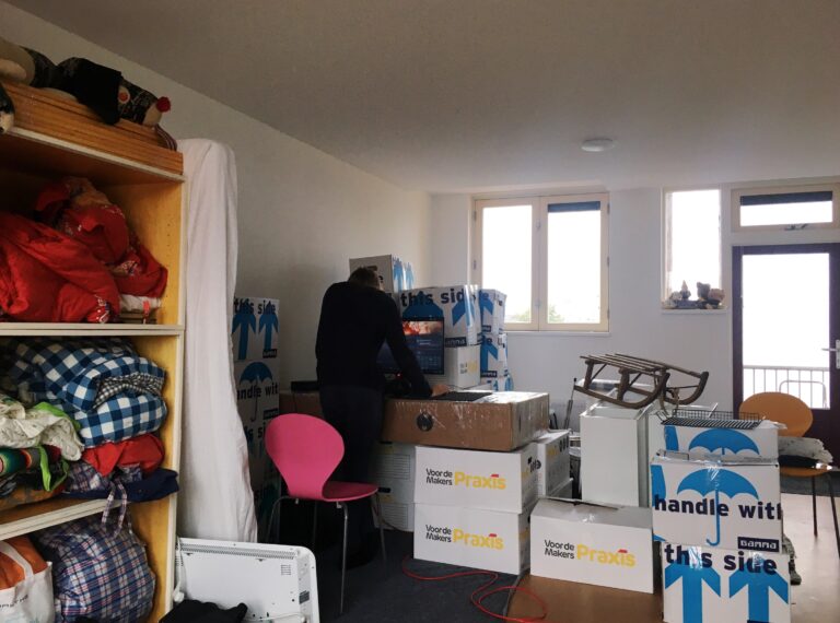 Een kamer vol met dozen en spullen in de kast links