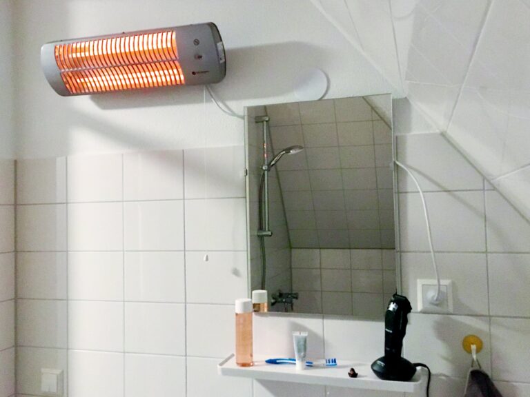 Linksboven aan de wand zit de infraroodkachel rechts zit de spiegel en daaronder wat handige spulletjes voor in een badkamer. In de spiegel reflecteert de douche 