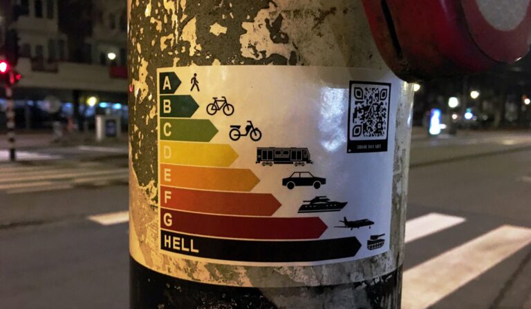 Een stikker op een stplichtpaal. Die de duurzaamheid aangeeft per manier van voortbewegen.:
A: lopen
B. fietsen
C. brommen / elektrische voortbeweging 
D: openbaar vervoer
E. auto
F. superjacht
G. vliegtuig
Hell: tank