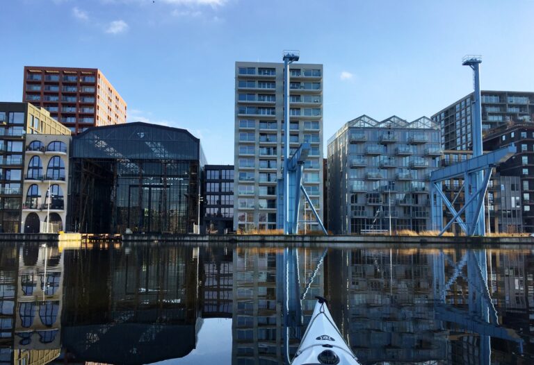 De moderne flatgebouwen op Oostenburg in Amsterdam vanaf het stille water op een zonovergoten dag. Het was vroeger een havengebied met werven, industrie en pakhuizen. Het heeft dat gevoel nog steeds maar dan worden de mensen opeengepakt.
