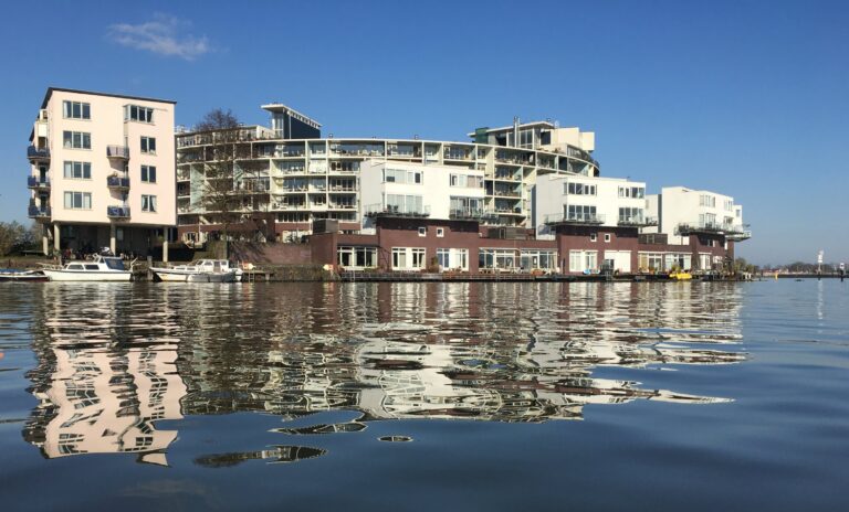 Het ronde witte gebouw aan de kop van het KNRM eiland (Venetiëlaan) in Amsterdam. Genomen vanaf het rustige water. Mooi contrast met de blauwe lucht en het spiegelende water