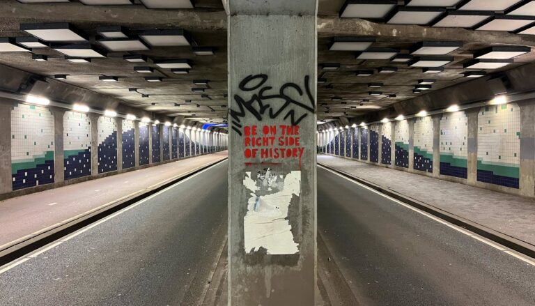 foto van de vierkante betonnen zuil in de tunnel met daarop de tekst in rode blokletters "Be on the right side of history". Daaronder een spoor van het weggescheurde pamflet.