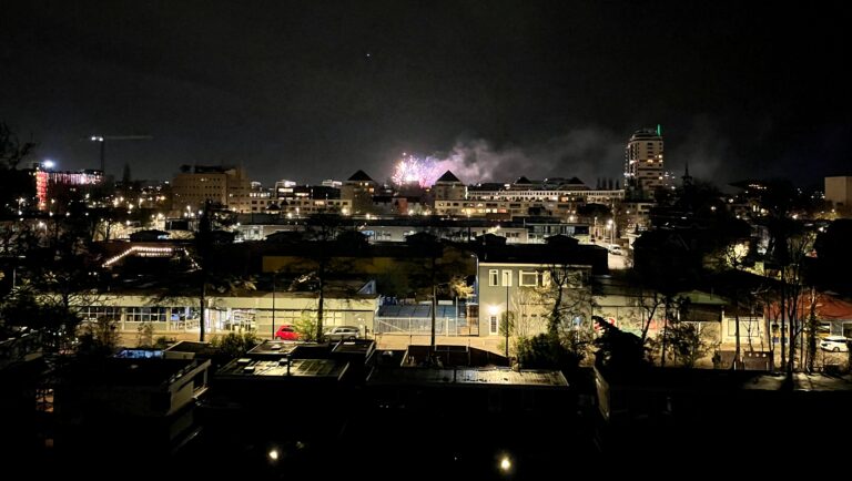 Foto van mijn uitzicht vanuit het raam op 4 hoog. Het is nacht maar de stad is nog veel verlicht. Op de horizon zie de wat vuurwerk en de rook die het genereerd.