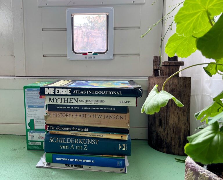 Het kattenluik in de deur zit hoog dus om de kat de kans te geven er doorheen te kunnen is er een stapel boeken. Dikke kunstboeken, de mythen van de mensheid, wonderen der wereld , history of our world en Die Erde atlas international.