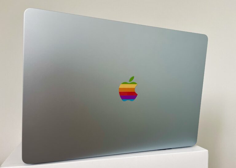 Een Apple macbook air met de klep open. Met daarop het oude regenbooklogo op de plaats van het reguliere spiegelende logo.
