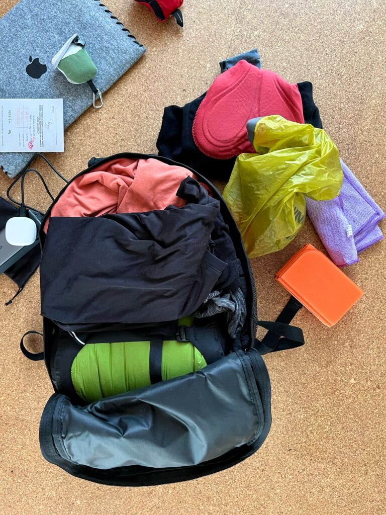 Een open ingepakte tas met allemaal spullen er omheen die er niet in gaan maar er wel in moeten.