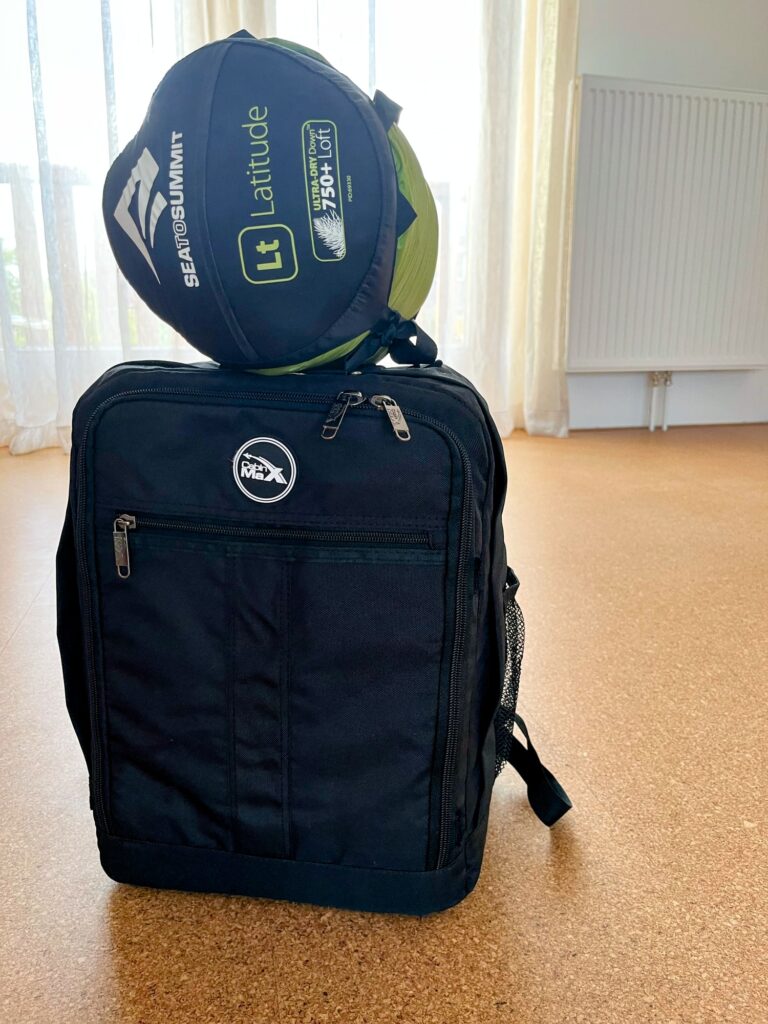 Een reistas met daar bovenop een ronde tas met ene slaapzak erin.