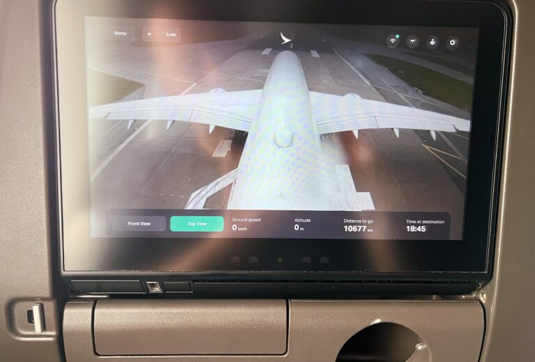 De monitor in de stoel van een vliegtuig. Het laat nu de camera viewpoint zien vanaf de staart van het vliegtuig en daaronder ground speed, altitude, afstand te gaan en aankomsttijd.