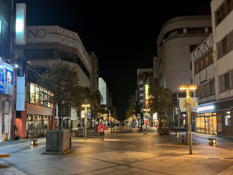 Breede winkelstraat in Asahikawa. Het is 19u en het is donker en rustig. Het is warm terwijl het toch al september is.