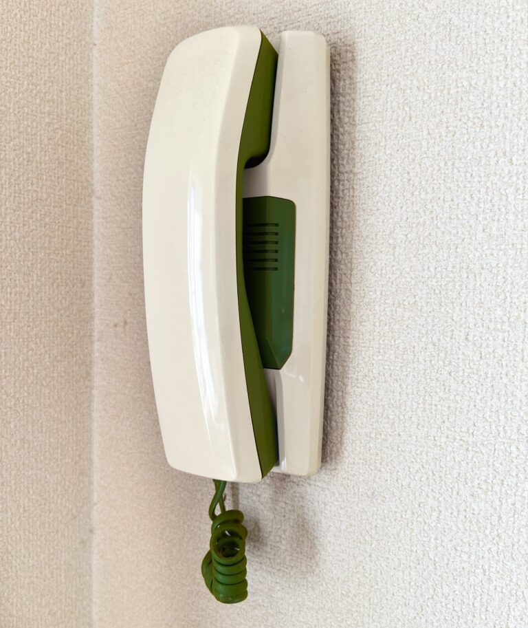 retro telefoon die aan de muur hangt. Hij is wit maar de binnenkant van de telefoon is groen.