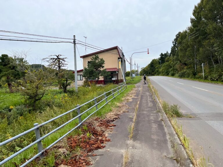 We fietsen de heuvel op langs de weg. Aan de linkerkant hier. links een huis rechts van de weg bomen.