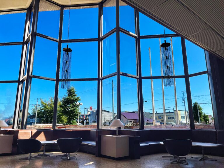 Uitzicht van de lobby van een hotel met een grote raampartij die voornamelijk de blauwe lucht laat zien.