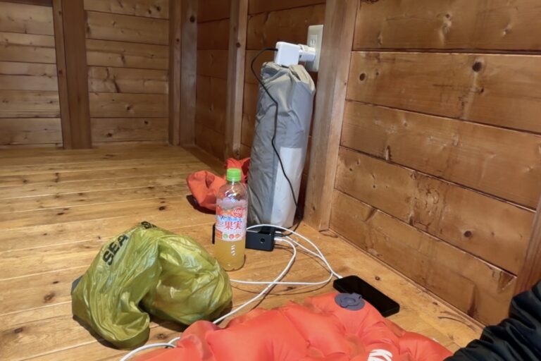 In een houten blokhut sit mijn adapter voor mijn laptop aan de stekker met de tenttas als ondersteuning zodat die erin blijft.