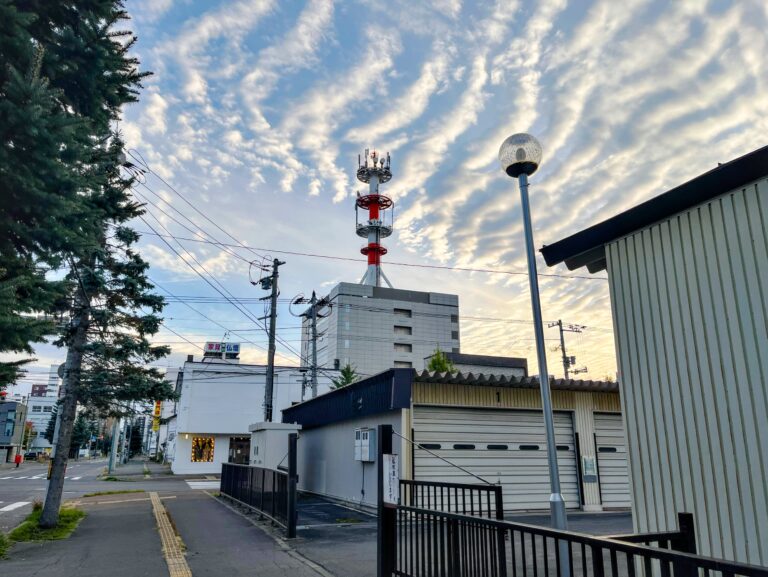Een rood witte mast op een grijs gebouw met daarboven wolken die lijken als golven.