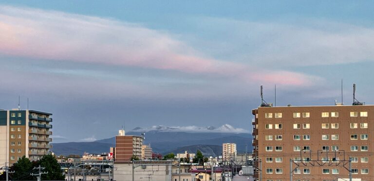 Uitzicht op besneeuwde bergtoppen tussen twee flatgebouwen in in een stads panorama