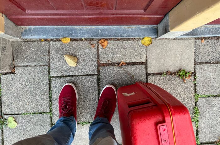 een foto van de plek waar ik sta. Op een stoep bij een rode voordeur met mijn rode schoenen en rode koffer rechts van me.